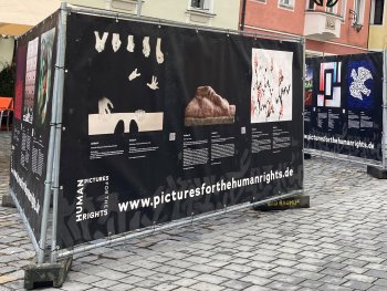 Copyright: Pictures fpr the Human Rights e.V.
An Bauzäunen aufgehängte Banner zeigen Bilder und Text zu der Allgemeinen Erklärung der Menschenrechte in einer Fußgängerzone.