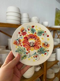 Eine Hand hält einen bunt verzierten Teller hoch. Es wurden rote Blumen mit grünen Blättern und kleinen Beeren gemalt.