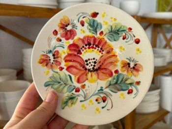 Copyright: Kateryna Chebotarova Eine Hand hält einen bunt verzierten Teller hoch. Es wurden rote Blumen mit grünen Blättern und kleinen Beeren gemalt.