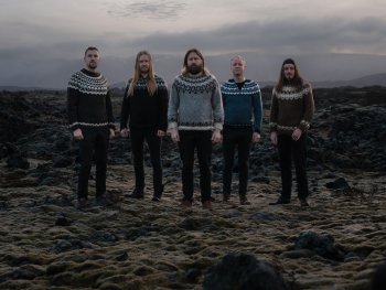 Fünf Personen stehen nebeneinander auf moosbedecktem, felsigem Boden und tragen traditionelle isländische Strickpullover mit verschiedenen Mustern