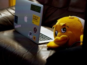 Ein Notebook mit Aufklebern auf einer Couch. Daneben ein Kuscheltier Fisch (Puffy das OpenBSD Maskottchen)