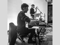 Mann spielt Keyboard + Frau spielt Klarinette auf Bühne, schwarz-weißes Bild