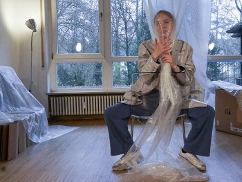 Foto: Theresa Muennich
Person sitzt breitbeinig auf einem Stuhl in einem Raum mit Holzboden und hält eine große Luftpolsterfolie