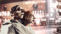 Zwei Figuren - im Hintergrund, die beleuchtete Hauswand einer Stadt