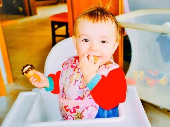 Kind sitzt im Hochstuhl und hält Essen in der Hand