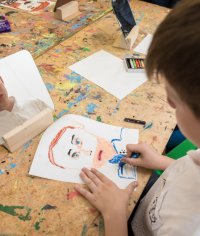 Ein Junge sitzt vor einem Spiegel und zeichnet auf ein Blatt Papier sein eigenes Porträt.