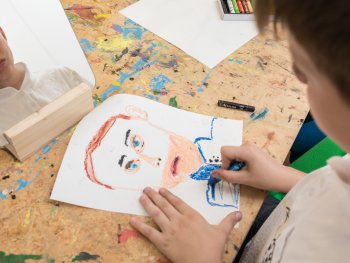 Ein Junge sitzt vor einem Spiegel und zeichnet auf ein Blatt Papier sein eigenes Porträt.