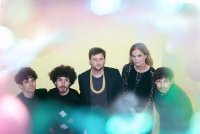 Fünf Personen in dunkler Kleidung vor einem hellen Hintergrund mit unscharfen bunten Lichtpunkten im Vordergrund