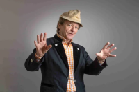 Erwin Pelzig breitet beide Arme aus und schaut abwägend in die Kamera.