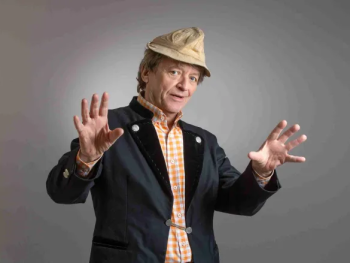 Erwin Pelzig breitet beide Arme aus und schaut abwägend in die Kamera.