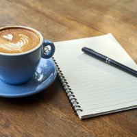 Kaffeetasse auf Unterteller neben linierten Block mit Stift