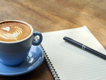 Kaffeetasse auf Unterteller neben linierten Block mit Stift