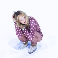 Person hockt im Schnee, trägt gepunkteten Pullover, Netzstrumpfhose und Sportschuhe