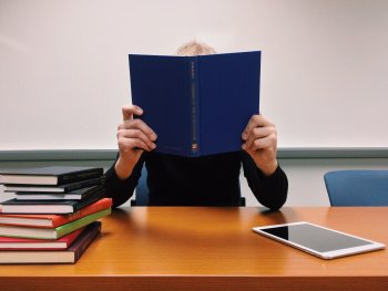 Ein Mensch hält ein aufgeschlagenes blaues Buch vor dem Gesicht