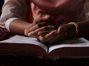 Gefaltete Hände über einem aufgeschlagenen Buch