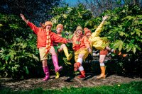 Die 4 Schauspielerinnen in bunter Kleidung und und bunter Gummistiefel stehen auf einem Bein