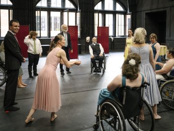 Foto: Sebastian Autenrieth
Gruppe von Menschen in einem großen Raum, einige im Rollstuhl, andere in eleganter Kleidung, die sich in einem Kreis versammeln