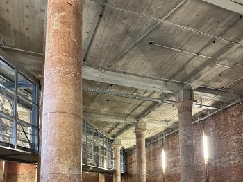 Foto: Astrid Betz
Vier Tänzer*innen in Rückenansicht tanzen nebeneinander, zwischen zwei großen Säulen aus Granit in einem großen Saal mit Steinmauern.