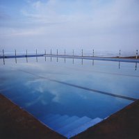 Swimmingpool in dem sich der Himmel spiegelt und im Hintergrund das Meer zu sehen ist