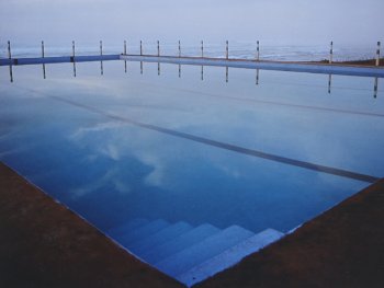 Swimmingpool in dem sich der Himmel spiegelt und im Hintergrund das Meer zu sehen ist