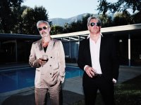 Zwei Männer in Anzügen stehen nebeneinander an einem Pool, jeder hält ein Glas in der Hand.