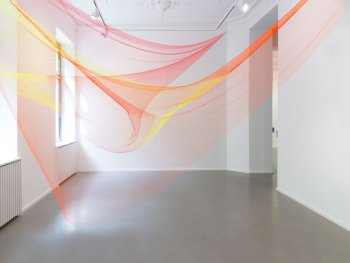 Copyright: Rana Begum, No. 1084 Net, 2021 Zwei Fischernetze in Orange und Gelb sind in einem Raum von Wand zu Wand gespannt.