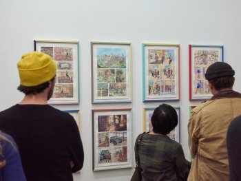 Drei Personen vor Bildern einer Ausstellung in Rückenansicht