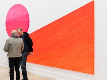 Copyright: Rupprecht Geiger, Pinc contra orange (I, II), 2005 Acryl auf Leinwand, zweiteilig, 275 x 470 cm Archiv Geiger, München; (c) VG Bild-Kunst Bonn, 2026 Zwei großformatige Gemälde: eine rote schiefe Ebene und ein pinkfarbener Kreis berühren sich an der Spitze der schiefen Ebene