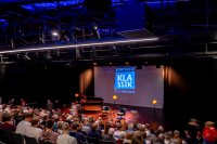 Bühne mit Klavier, zwei Stühlen und Leinwand mit Schriftzug 'KONTRASTE KLASSIK IN DER TAFELHALLE' vor Publikum in einem Theaterraum