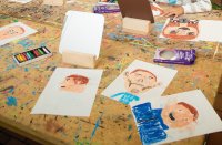 Auf einem Tisch liegen 5 Zeichnungen mit gezeichneten Selbstporträts.