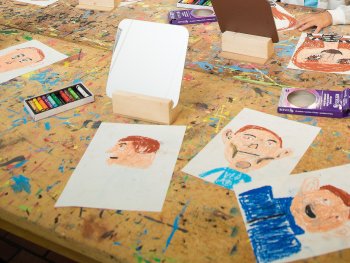 Auf einem Tisch liegen 5 Zeichnungen mit gezeichneten Selbstporträts.