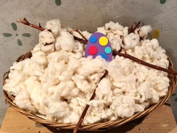 Foto: Ingrid Moor
In einem Flechtkörbchen, das mit unbehandelter Schafwolle gefüllt ist, liegt mittig ein buntes gebasteltes Osterei.