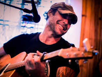 Ein Mann mit Cap und Akustikgitarre hinter einem Mikrofon
