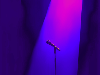 Ein Scheinwerfer wirft Licht auf ein Mikrofon. Alles ist in blau und lila Farbe gehalten.