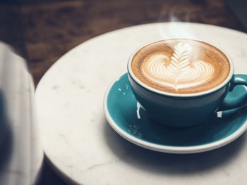 Dampfender Kaffee in blauer Tasse auf Untertasse und Tisch