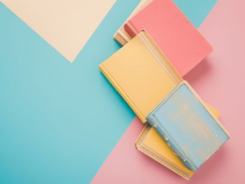 Stapel pastellfarbene Bücher liegen auf pastellfarbenem Untergrund