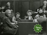Schwarz-weiße Aufnahme eines Gerichtssaals mit mehreren Personen, die an Tischen sitzen,