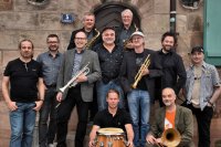 Das Foto zeigt elf Bandmitglieder der Band HOT CARGO, teilweise mit Instrumenten in den Händen.