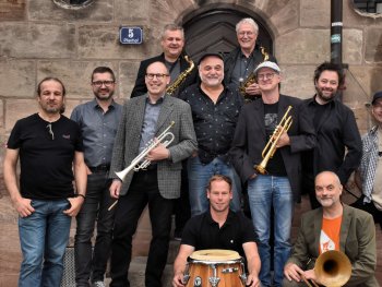 Foto: Peter Kick
Das Foto zeigt elf Bandmitglieder der Band HOT CARGO, teilweise mit Instrumenten in den Händen.