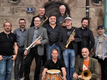 Das Foto zeigt elf Bandmitglieder der Band HOT CARGO, teilweise mit Instrumenten in den Händen.