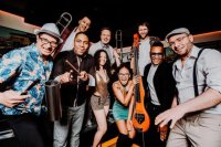 Das Foto zeigt die Bandmitglieder der Band Román y sus Timberos fröhlich und mit ihren Instrumenten.