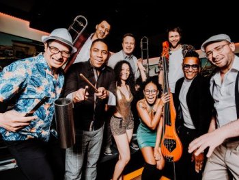 Das Foto zeigt die Bandmitglieder der Band Román y sus Timberos fröhlich und mit ihren Instrumenten.