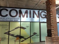 Großflächige Fensterfront mit Schriftzug »COMING SOON« und Texten zu einer Ausstellung 2026, davor zwei gemauerte Säulen in einem Betonraum.