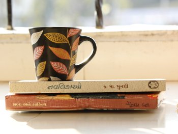 Eine schwarze Tasse mit Blättermuster steht auf zwei Büchern vor einem Fenster