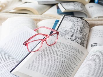 Eine rote Brille liegt mittig auf mehreren aufgeschlagenen Büchern