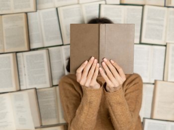 Foto: Pixabay
Eine Person in einem ockerfarbenen Pullover hält sich mit beiden Händen ein Buch vor das Gesicht. Die Person liegt auf vielen aufgeschlagenen Büchern.