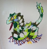 Eine gestickte bunte Fantasie-Kreatur mit grünem Körper und geschwungenem Schwanz.