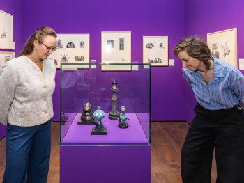 Zwei Besucherinnen stehen neben einer Glasvitrine und betrachten die ausgestellten Figuren aus Walter Moers Büchern.