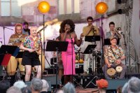 Eine Jazz-Band mit sieben Musikern auf einer beleuchteten Bühne spielt vor Publikum.