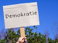 Eine Hand hält ein Schild mit dem Schriftzug "Demokratie" in die Höhe.